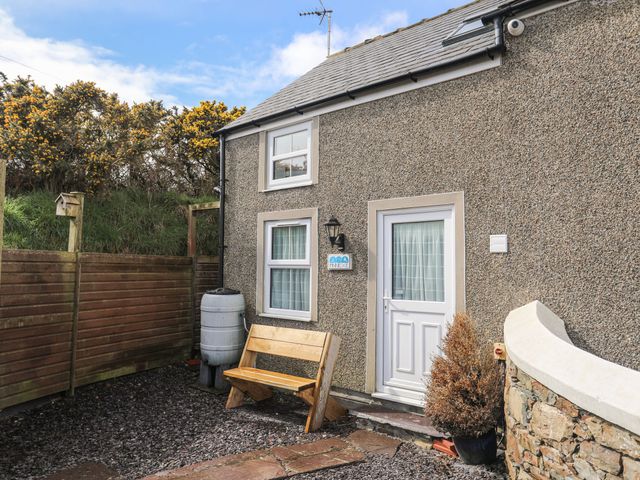 Exterior of a building with two windows a door a wooden bench a rain barrel a potted plant and a wooden fence at Mur Cwpwl - Annex in Cilan near Abersoch