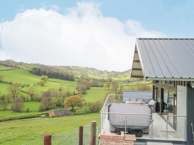 A balcony with outdoor seating and hot tub overlooking green hills and fields at Barcud Coch - Red Kite in Garthmyl