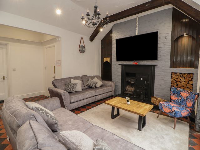 A living room with two gray sofas a wooden coffee table a patterned armchair a fireplace and a wall-mounted television at The Furness Haven in Barrow-In-Furness