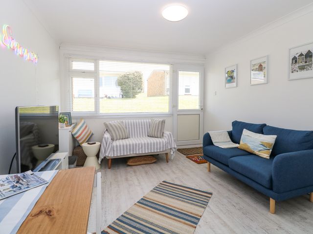 A living room with blue and striped sofas a television and framed pictures on the wall at Dolly's Lookout in Kessingland