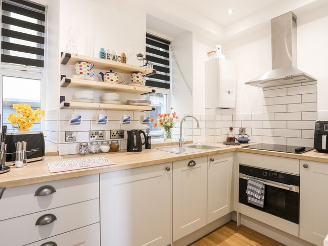 A kitchen with white cabinets wood countertops shelves with cups and plates flowers in vases and stainless steel fixtures at The Nook in Criccieth