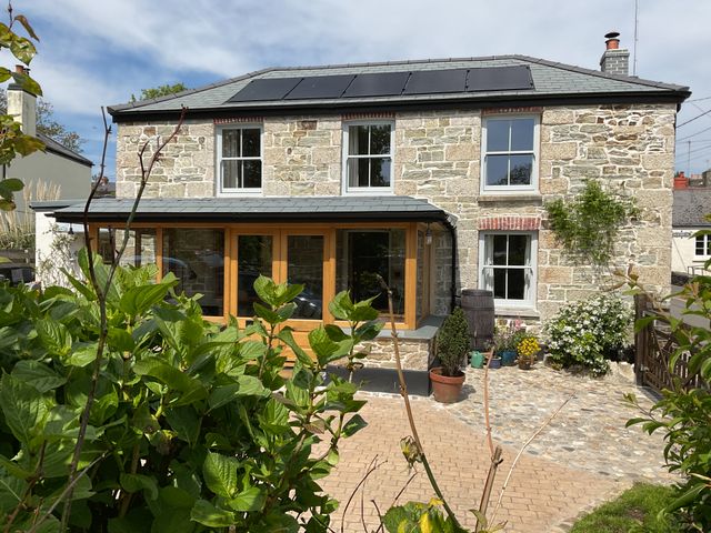 A stone house with solar panels on the roof and a garden with plants and flowers at Woodbine Cottage in Mylor Bridge Nr Falmouth