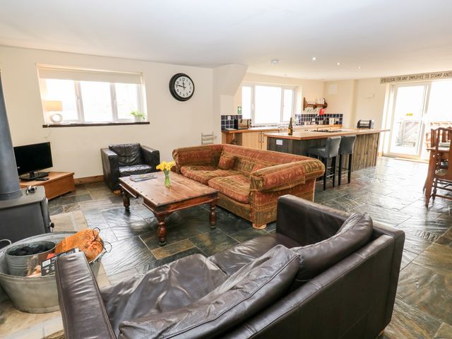 An open plan living area with sofas a wooden coffee table kitchen island with stools and dining table at The Bike Shed in New Mills