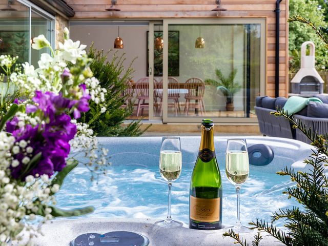 A hot tub with a bottle of cava and two glasses surrounded by plants next to a house with sliding glass doors and a dining table at 2 The Croft in Skipton