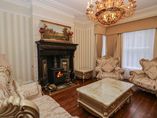 A living room with a fireplace armchairs a marble coffee table and a chandelier at Beechgrove Manor in Workington
