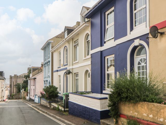 A street with colorful two-story houses and plants along the sidewalk at 27 Exeter Street in Teignmouth