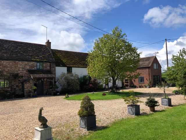 A gravel driveway with potted plants leading to a group of brick and white cottages with trees around at Little Stables Cottage in Spetisbury