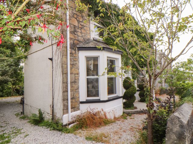 A stone and stucco house with a bay window surrounded by plants and gravel at Sea View in St Austell