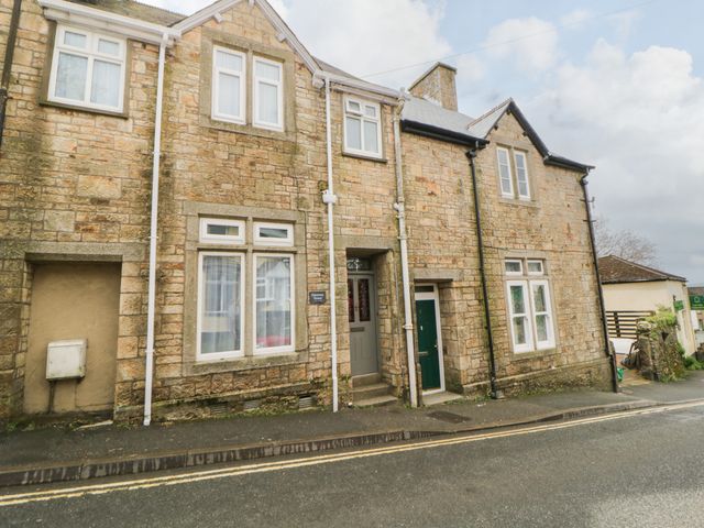 A street view of a stone house with multiple windows doors and a sign reading Harmney House in Bere Alston