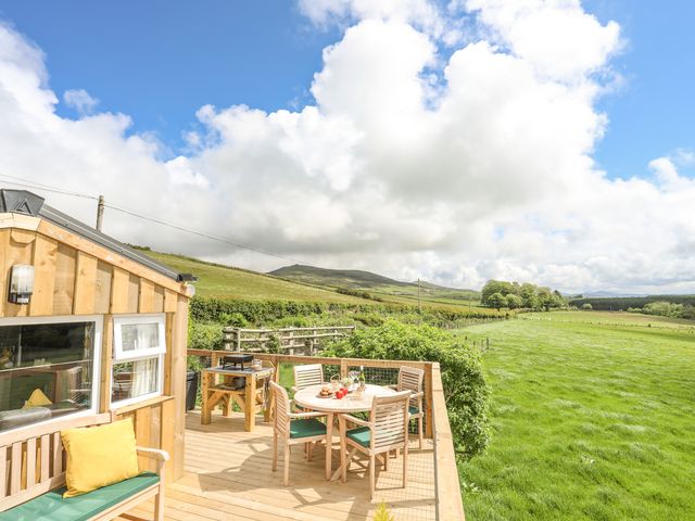 An outdoor wooden deck with a table and chairs next to a grassy field at Caban Cwtch The Cosy Cabin in Llanaelhaearn