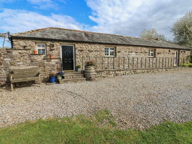 A stone cottage with a bench and flower pots at Rainbow Cottage in Kirkby Stephen