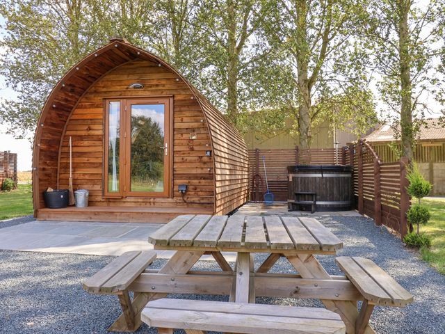 A wooden pod with glass door a picnic table and a hot tub in a fenced garden at Mischief in Little Kelk near Bridlington