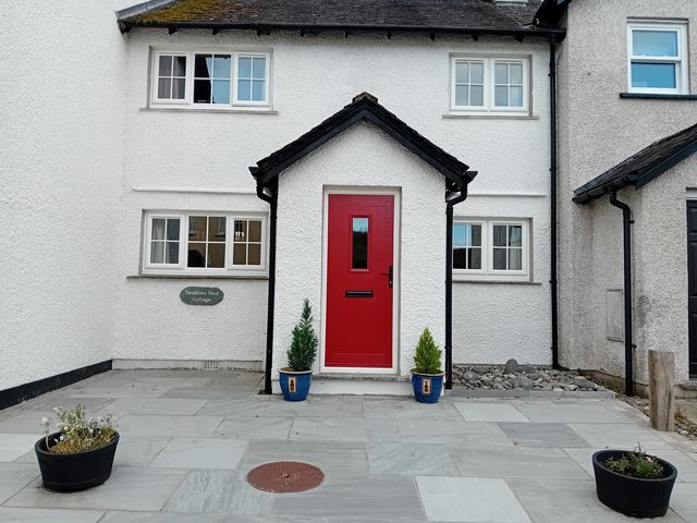 An exterior view of Swallows Nest Cottage in Hawkshead with red door and plants by the entrance