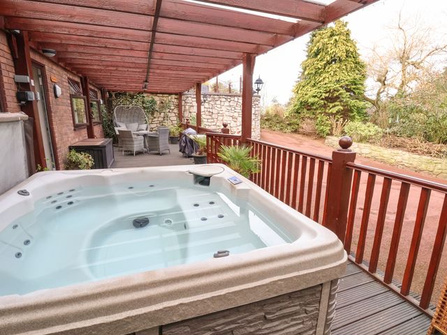 An outdoor covered patio with a hot tub a seating area and wooden railing at Acorns in Holywell