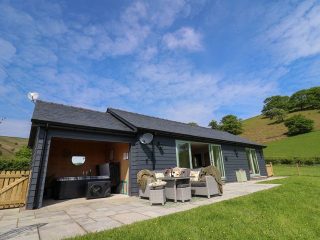 A patio area with outdoor seating and a hot tub attached to a single-story house in a rural setting at Dol Blodau in Newbridge-On-Wye