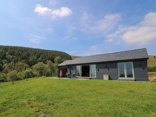 A single-story dark house with green doors and a grassy lawn at Ystrad Wen in Llysdinam near Newbridge-On-Wye