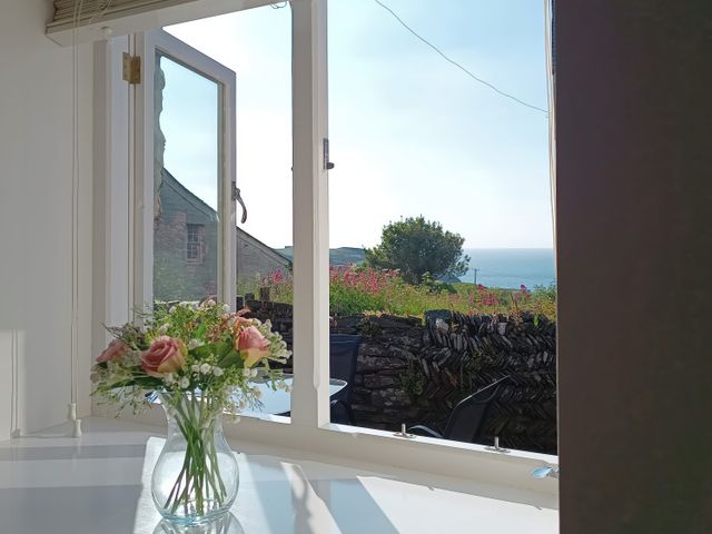 A vase with flowers on a table near an open window showing a garden wall and sea view at The Mill in Trethevy near Tintagel
