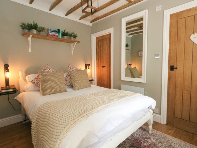 A bedroom with a bed pillows a shelf with plants and books a mirror and wooden doors at Apple Tree Cottage in Upton near Ringstead Bay