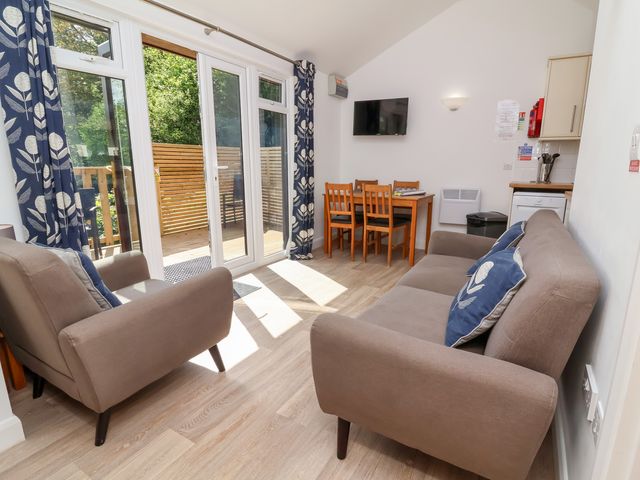A living area with two armchairs and a sofa near glass doors and a dining table with four chairs at Chalet Log Cabin C9 in Combe Martin