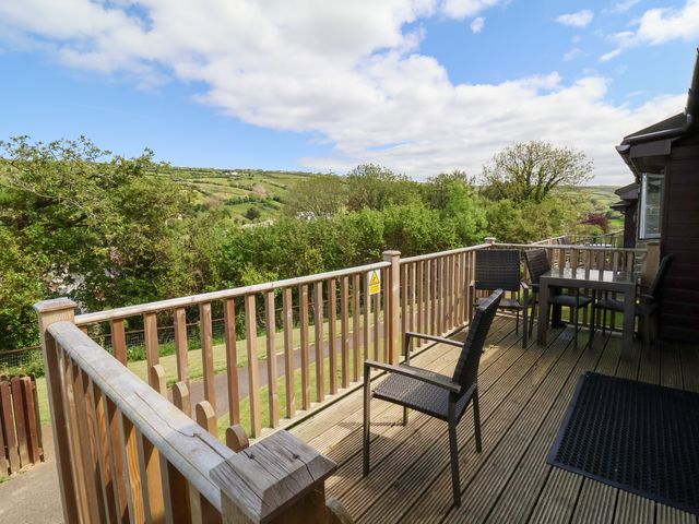 A wooden deck with black chairs and a table overlooking green trees and hills at Chalet Log Cabin L12 in Combe Martin