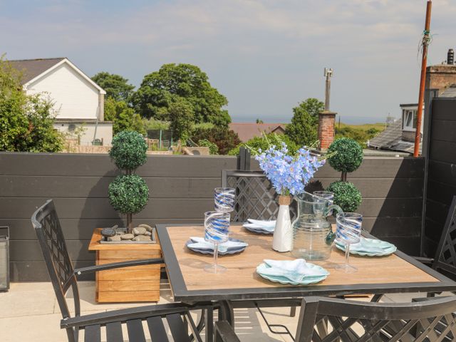 An outdoor patio with a wooden table set with plates glasses a water pitcher and a vase of blue flowers at Brigwyn in Nefyn