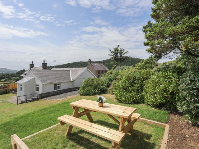 A wooden picnic table with a flower pot on grass with houses and trees in the background at Glan Awel in Nefyn