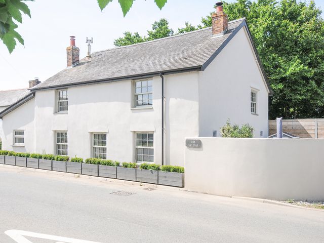 A white two story cottage with multiple windows and planters in front at Cob Cottage near Rock