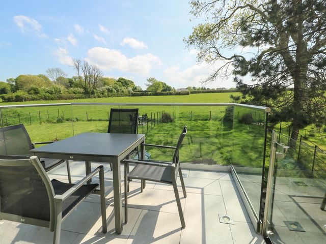 An outdoor balcony with black table and chairs overlooking a green field with trees at Gwalia Cottage in Brynsiencyn
