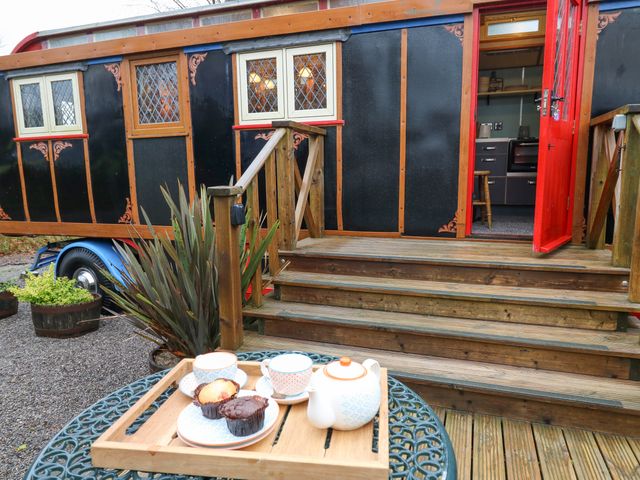 A wooden trailer with a red door and stairs leading up to it with tea set and muffins on a table outside Dolly the Circus Wagon in Brynhoffnant