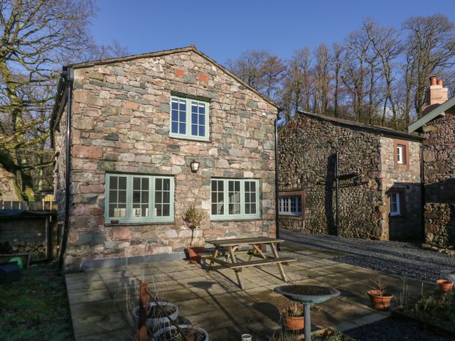 A stone house with green windows and a wooden picnic table on a paved patio at The Barn in Nether Wasdale