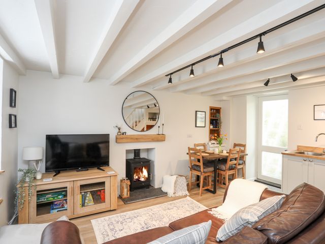 A living room with a TV on a wooden cabinet a fireplace a round mirror a dining table with chairs and a brown sofa at Bwthyn Lili in Cemaes Bay