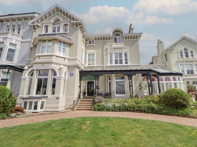 A large house with multiple windows and a covered porch with iron supports surrounded by a garden and lawn at Ismay Dining Room Suite - Titanic Interest in Waterloo Merseyside