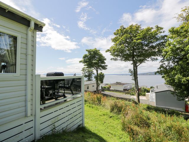 A view of a grassy hillside with trees and several mobile homes overlooking a body of water at Olivias Haven in Wemyss Bay
