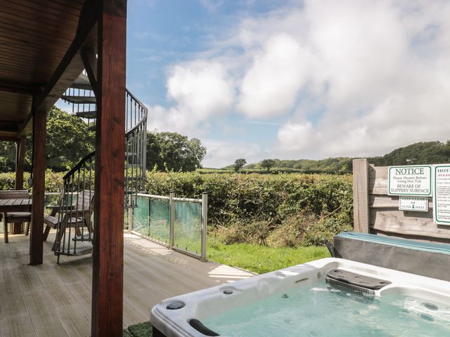 An outdoor wooden deck with a hot tub a spiral staircase and a picnic table surrounded by greenery at Ash Swanage