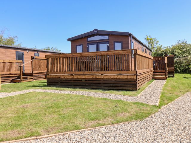 A wooden mobile home with a fenced deck on a grassy plot with gravel paths at Foxglove Lodge in Runswick Bay near Staithes