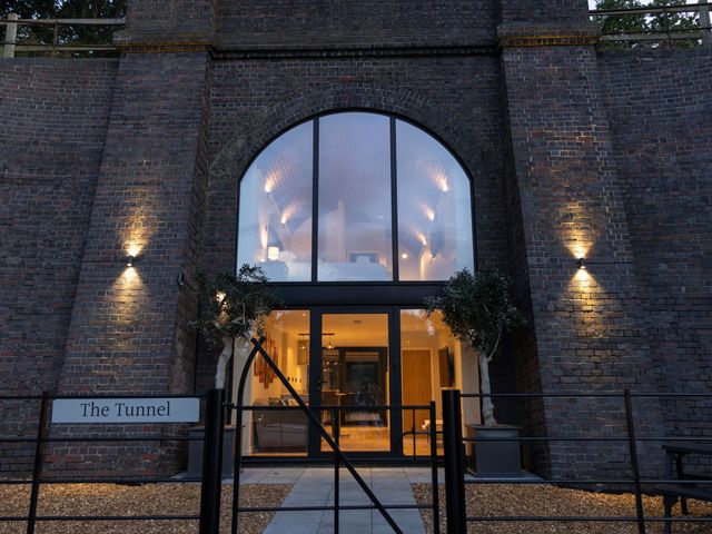 An exterior view of a brick building with large arched window and glass door with two potted plants on either side at The Tunnel at Bridge Lake Farm and Fishery in Chacombe