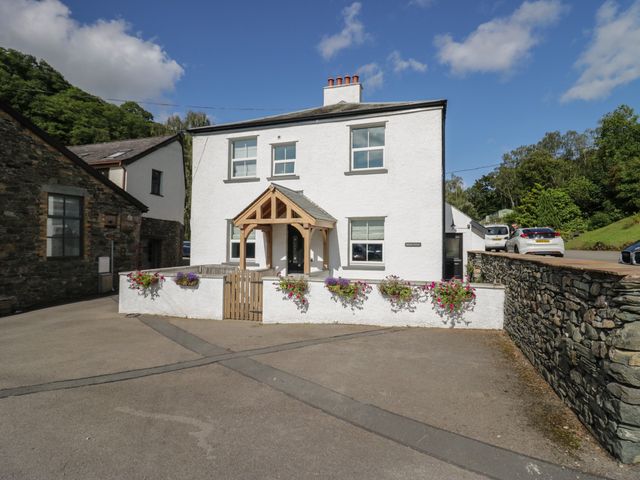 A white two-story house with a wooden porch and flower boxes in front surrounded by a stone wall at Briery House in Keswick