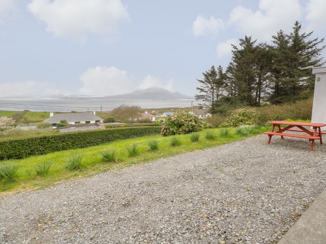 A gravel patio area with a red picnic table overlooking a grassy garden with shrubs and trees at Sea View House in Tully County Galway