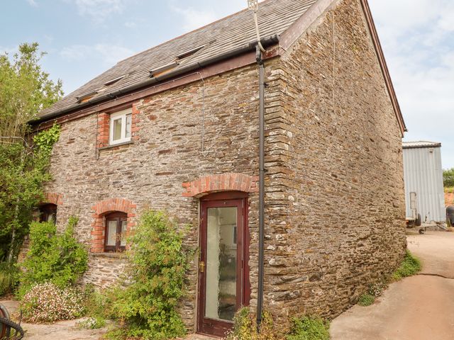 Exterior view of a stone barn with a glass door and small windows surrounded by plants at Higher Norton Barn in East Allington Devon