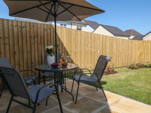 A patio with glass table umbrella four chairs and wooden fence at Pebble Bay in Appledore