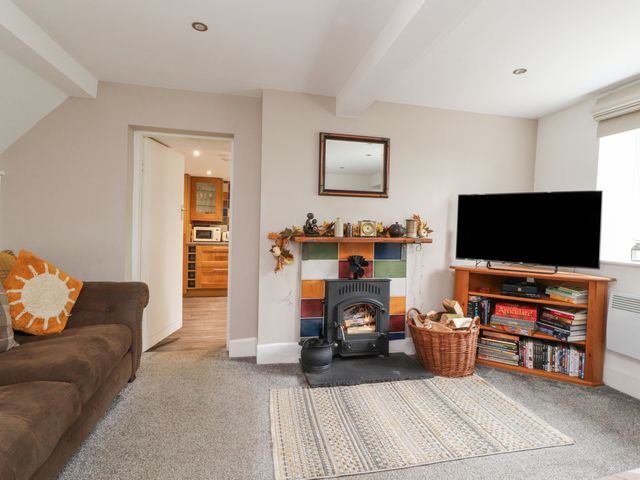 A living room with a brown sofa a fireplace with colorful tiles a television on a wooden stand and a basket of firewood at Stork Cottage in Conder Green near Glasson
