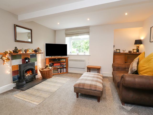 A living room with a fireplace a television a brown sofa and a plaid ottoman at Stork Cottage in Conder Green near Glasson