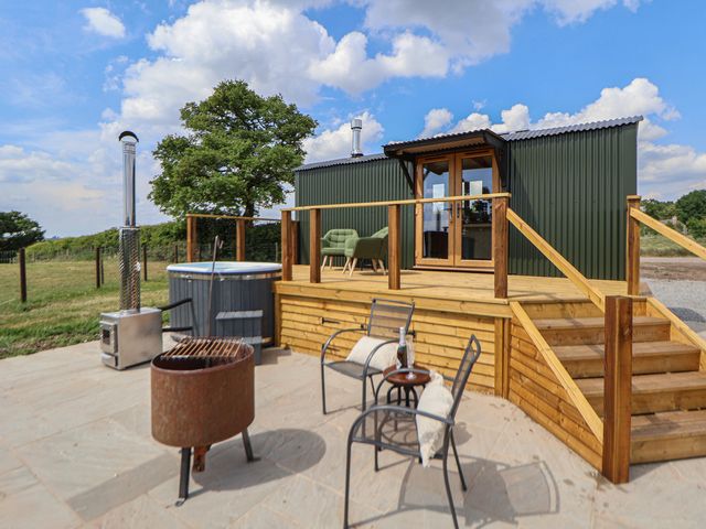 An outdoor patio with chairs a fire pit hot tub and a wooden deck at The Coop in Aston near Woore
