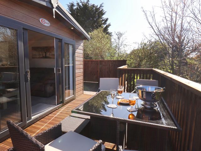 An outdoor wooden deck with a glass-top table and four chairs with drinks and snacks at Marigold Lodge in Runswick Bay near Staithes