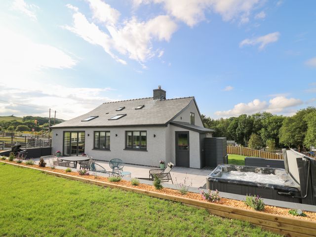 A house with a patio featuring outdoor furniture and a hot tub with a grassy yard at Rhiwmynach in Pontarfynach near Aberystwyth