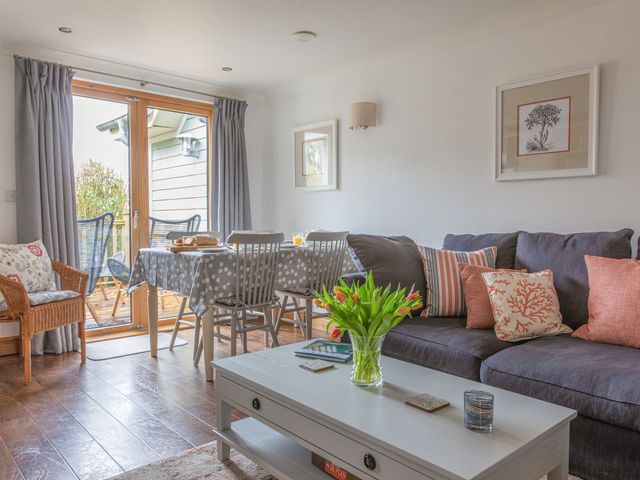 A living room with a gray sofa and a white coffee table with flowers and books and a dining table with chairs near glass doors leading to an outdoor area at 5 Court Cottage Hillfield Village in Dartmouth