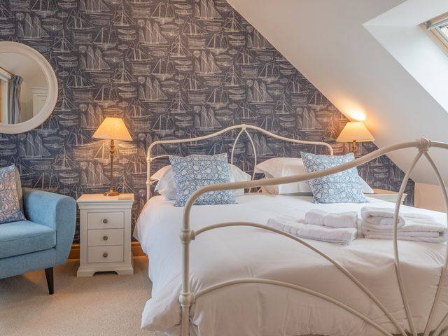 A bedroom with a white metal bed frame blue patterned pillows bedside tables with lamps and a blue armchair at 5 Court Cottage Hillfield Village Dartmouth