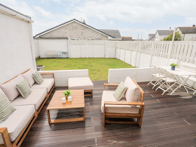 A backyard with wooden deck furniture and a grassy lawn at 31 Sisial Y Mor in Rhosneigr