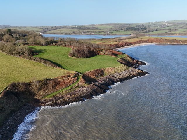 A coastal landscape with grassy fields rocky cliffs and a curved beach at Traeth Ora in Moelfre