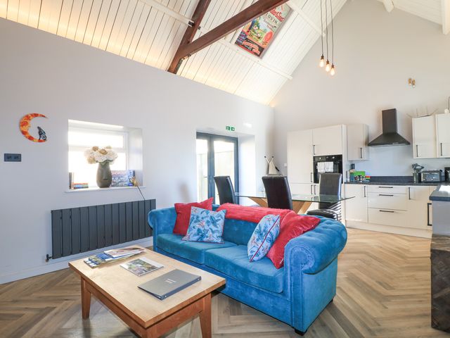 An open plan living room and kitchen with a blue sofa and glass dining table at Mayfield Cottage in Nr Malmesbury